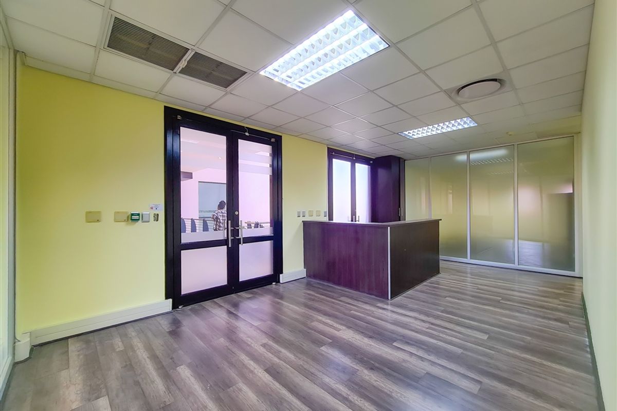A professional office space featuring laminate flooring, a built-in reception desk, frosted glass partitions, and a suspended ceiling with recessed lighting.