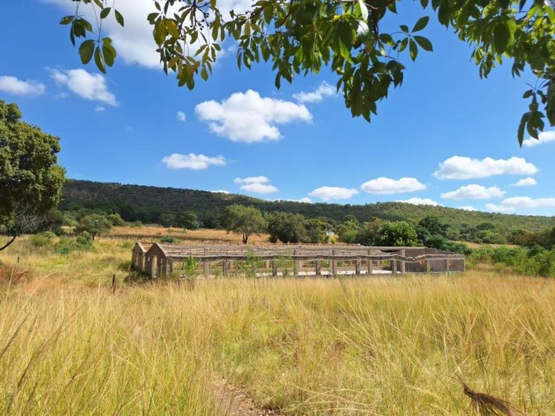An unfinished concrete structure set within a rural farm landscape, showing the primary structural frame and masonry walls of a building under development.