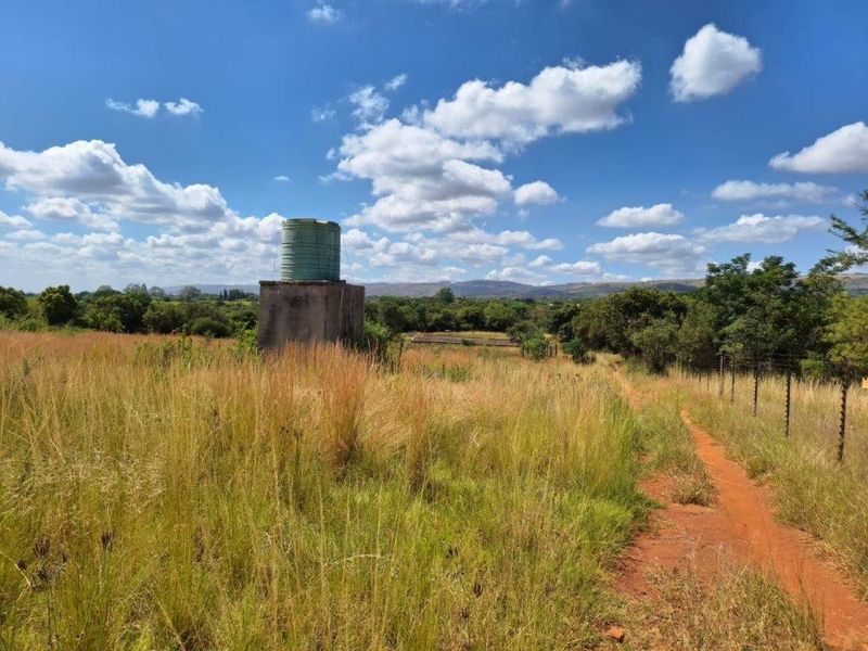 Open farm land featuring a raised water tank on a concrete stand and perimeter electric fencing with distant mountain views.