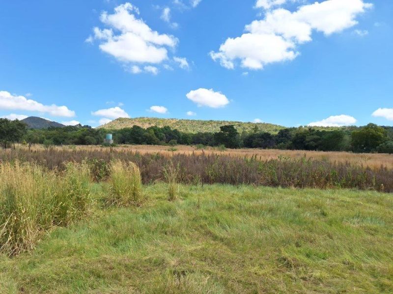 A scenic view of the farm landscape featuring open fields, natural vegetation, and a distant water tank under a clear blue sky.