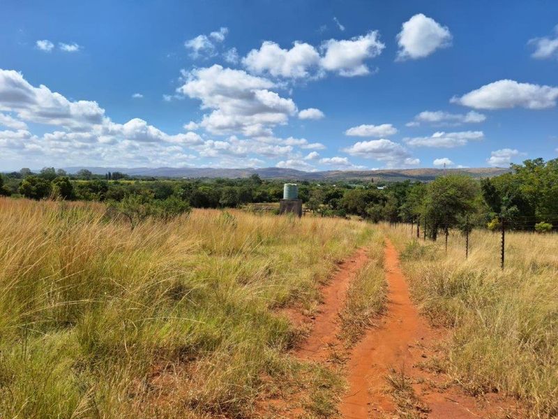 Expansive rural landscape view featuring a dirt access track, natural grassland, and a functional water storage tank on the property.
