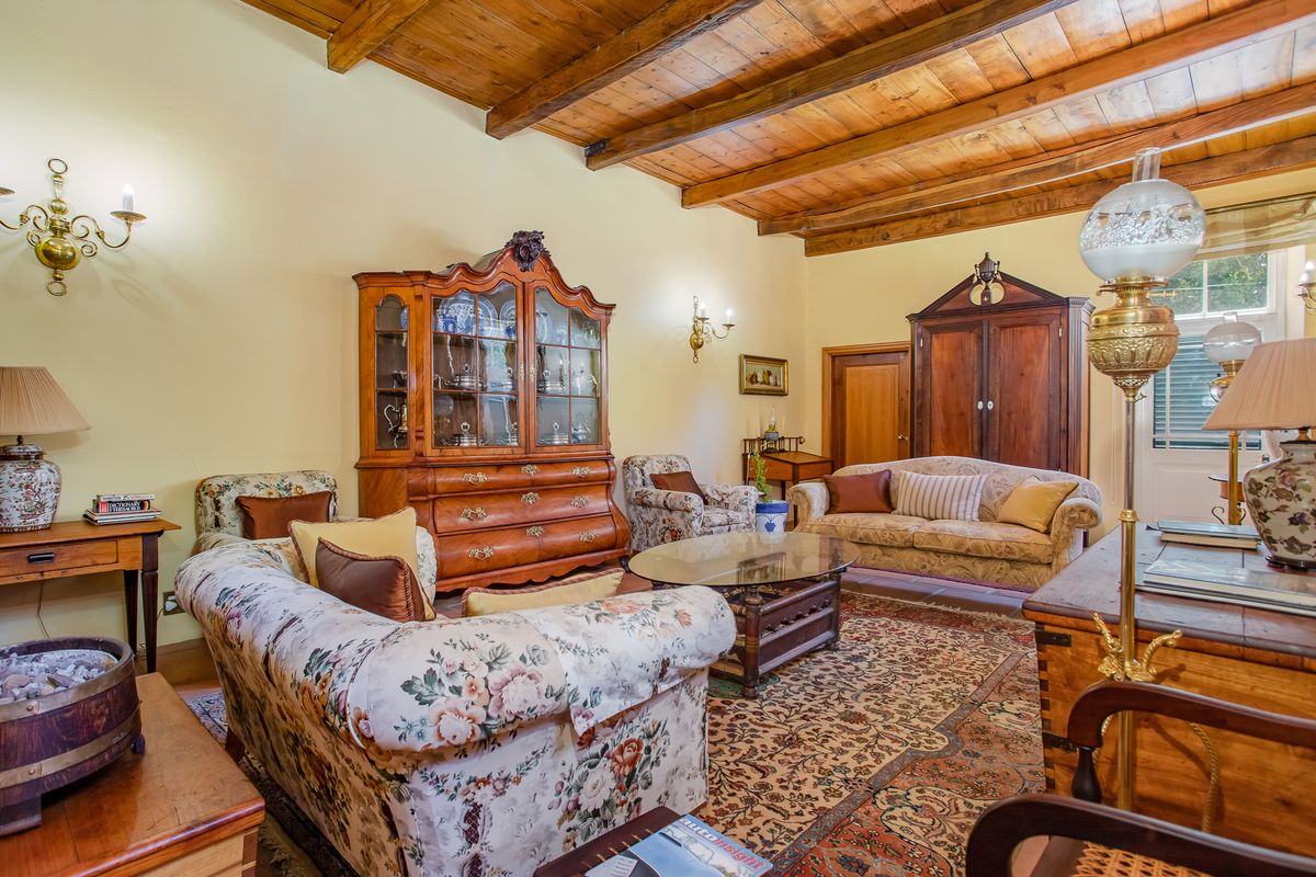A spacious living room featuring high exposed timber beam ceilings and warm wall lighting, creating a traditional and inviting atmosphere.