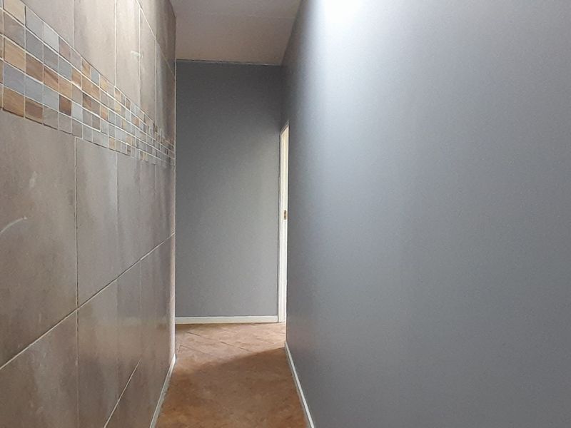 A clean, empty hallway featuring neutral grey walls, decorative ceramic wall tiling, and durable tiled flooring.