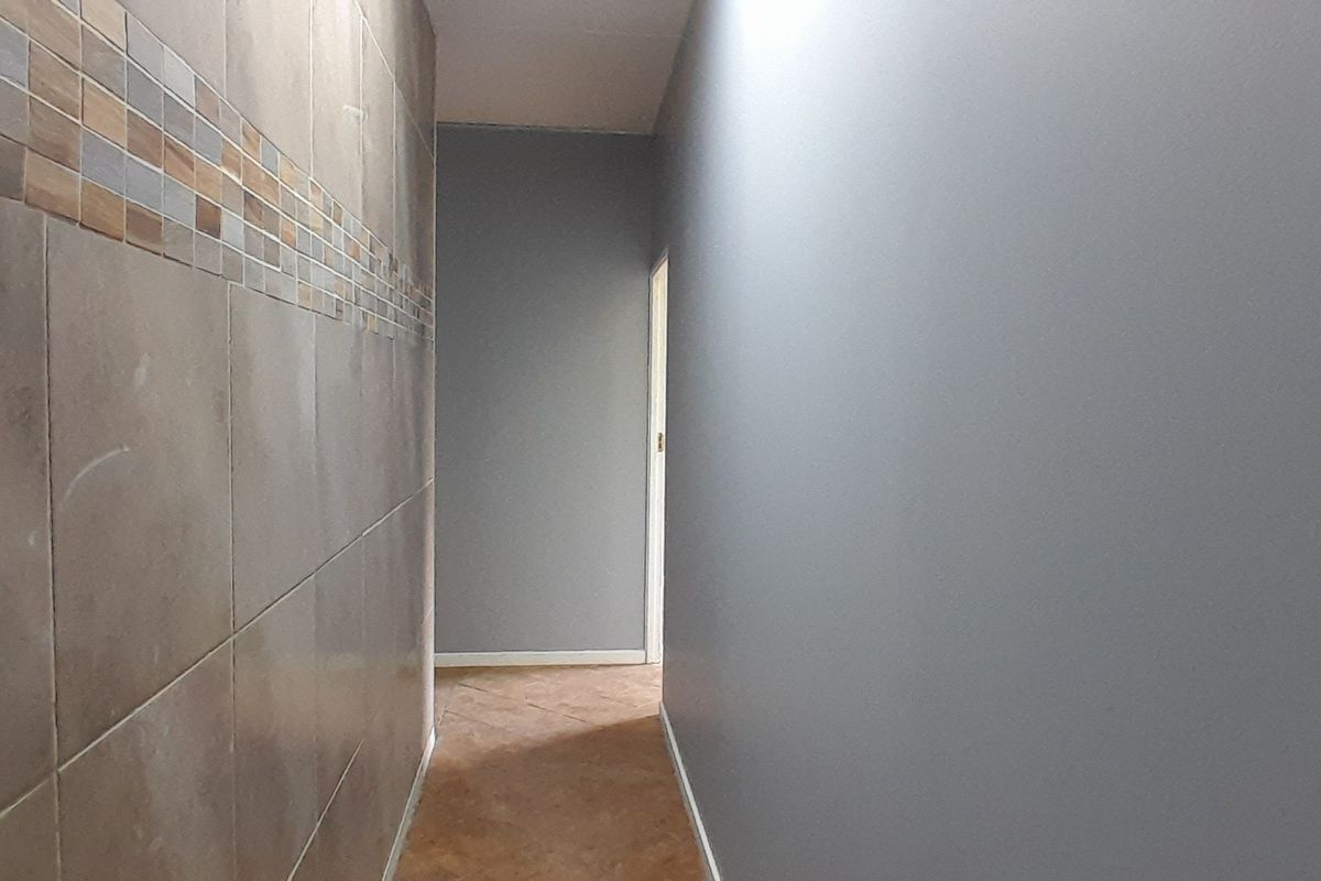 A clean, empty hallway featuring neutral grey walls, decorative ceramic wall tiling, and durable tiled flooring.