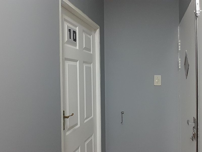 A simple office hallway featuring grey painted walls, white panelled doors, and a small section of decorative wall tiling.