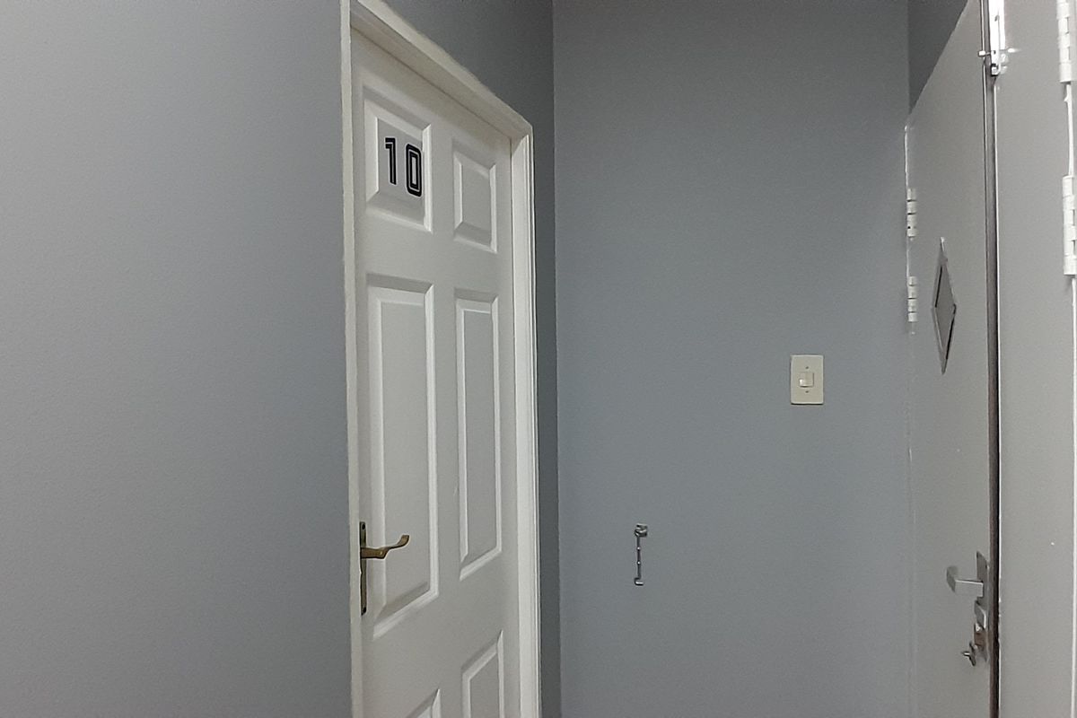 A simple office hallway featuring grey painted walls, white panelled doors, and a small section of decorative wall tiling.