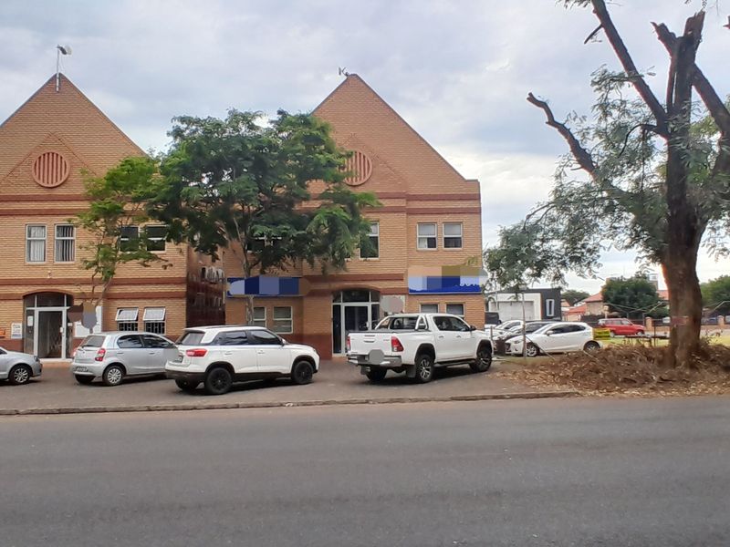 Front exterior view of a two-story brick office building featuring a gabled roof design and an adjacent paved parking area.