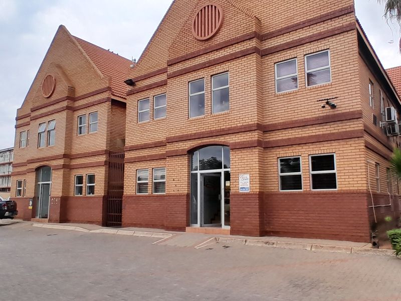 Front exterior view of a multi-story brick office building featuring a paved driveway, tiled roof, and aluminum-framed windows.