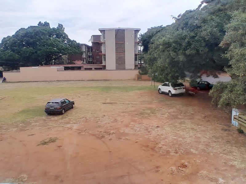 An elevated view of the property's rear grounds, featuring an unpaved parking area, perimeter wall, and mature trees.