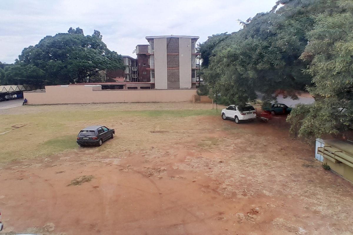 An elevated view of the property's rear grounds, featuring an unpaved parking area, perimeter wall, and mature trees.
