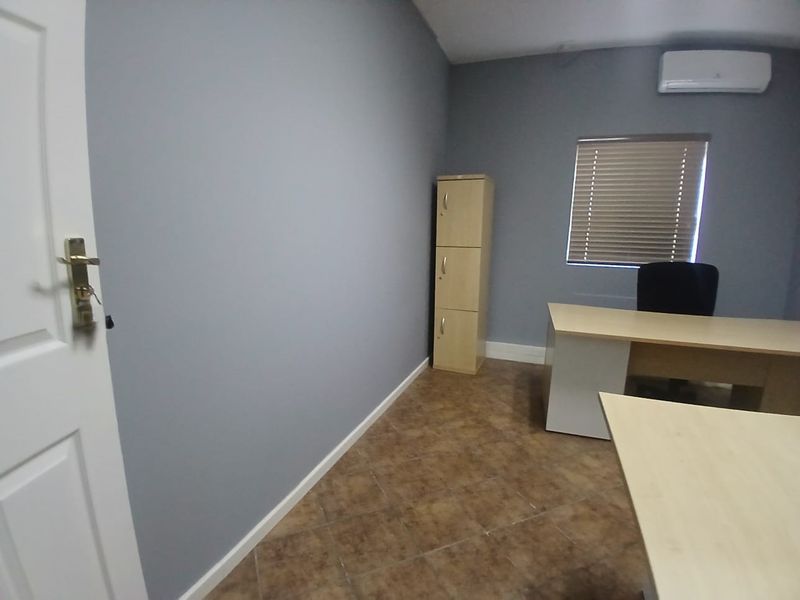 A functional office space featuring grey walls, tiled flooring, an air conditioning unit, and window blinds, providing a clean and professional work environment.