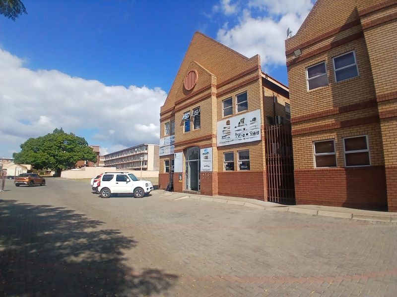 A view of the front facade of a face brick office building with a paved parking area and secure entrance.