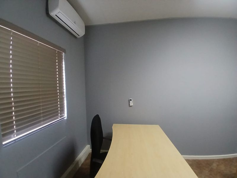 A functional office space featuring grey walls, tiled flooring, venetian blinds, and a wall-mounted split-system air conditioner.