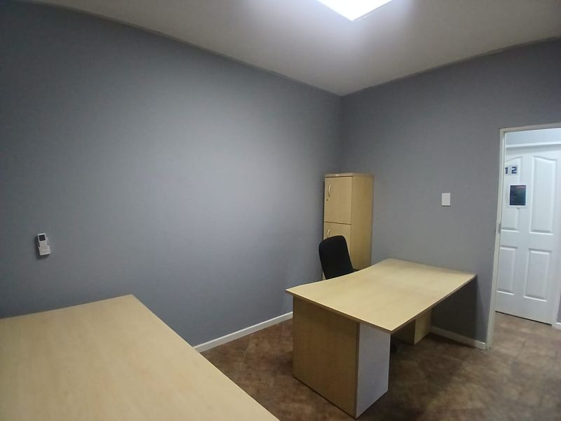 A functional office space featuring grey walls, tiled flooring, and a skylight providing natural illumination.