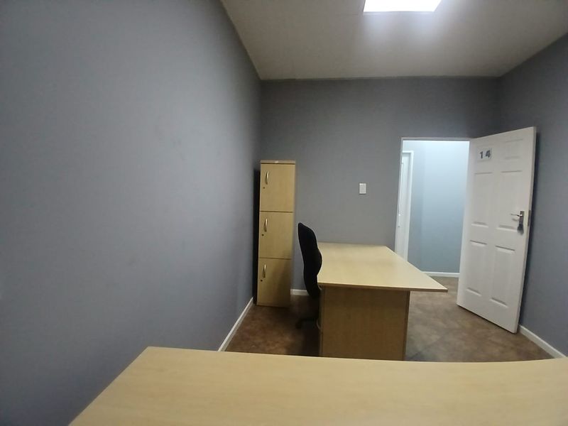 A functional office space featuring grey painted walls, tiled flooring, and a standard panel door, suitable for a professional work environment.