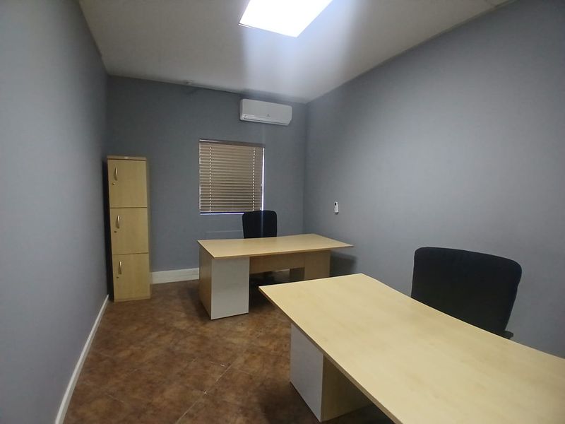 A functional office space featuring tiled flooring, an integrated air conditioning unit, and window blinds, providing a professional work environment.
