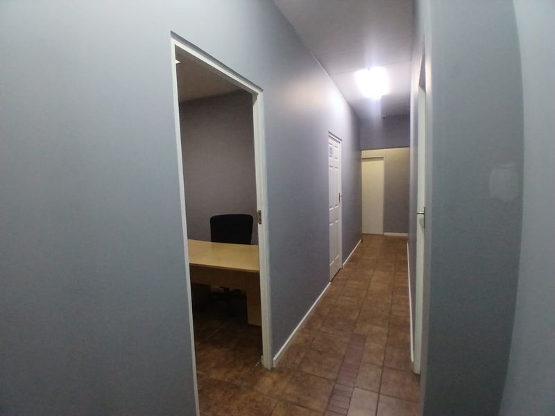 A functional office hallway with tiled flooring, neutral grey walls, and access to multiple office rooms.
