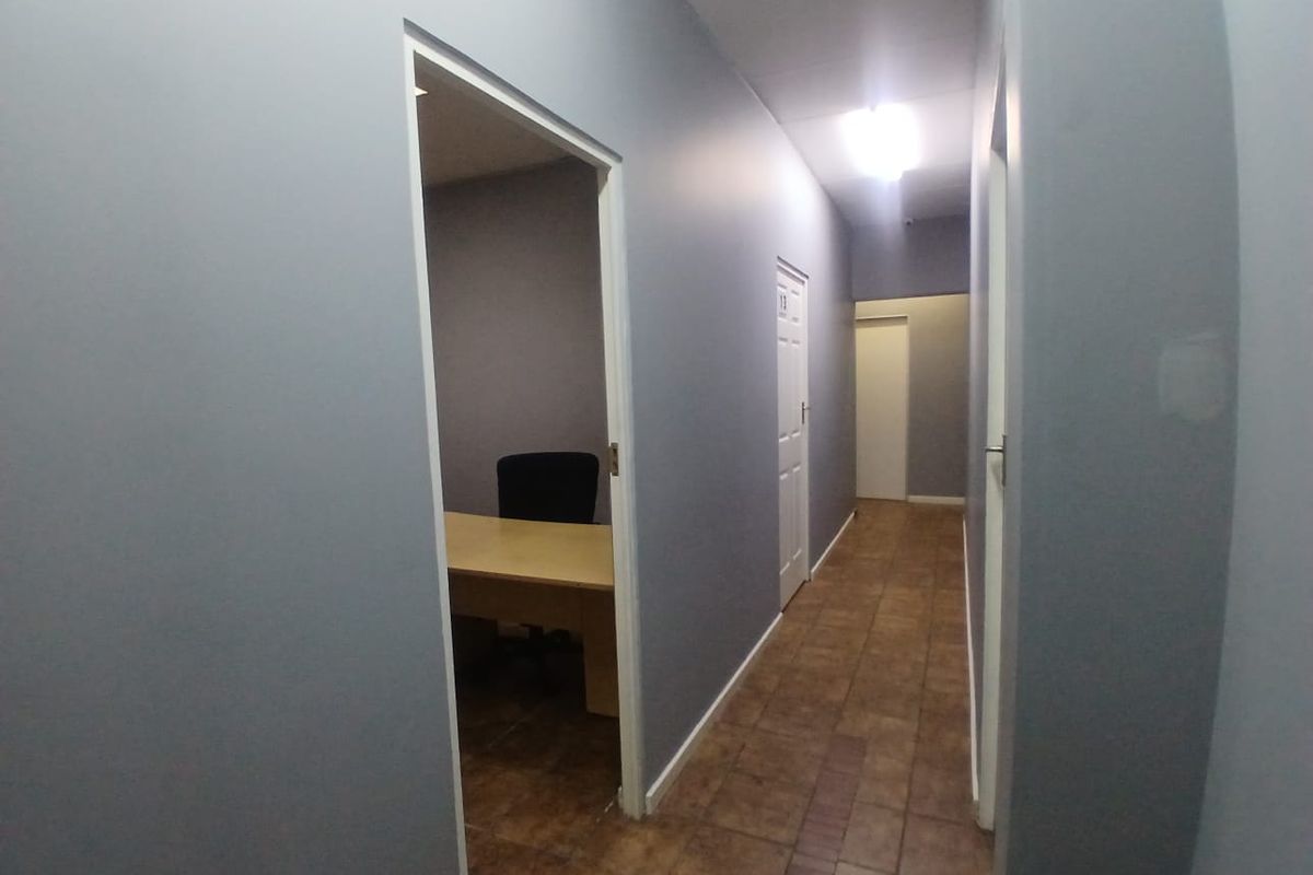 A functional office hallway with tiled flooring, neutral grey walls, and access to multiple office rooms.