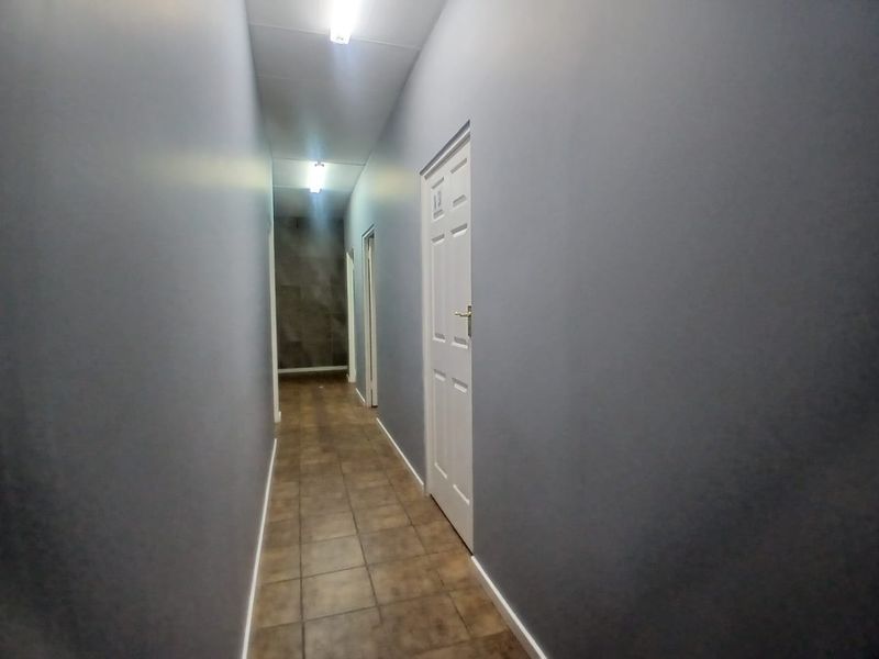 A clean, empty office hallway featuring grey painted walls, tiled flooring, and multiple access doors.