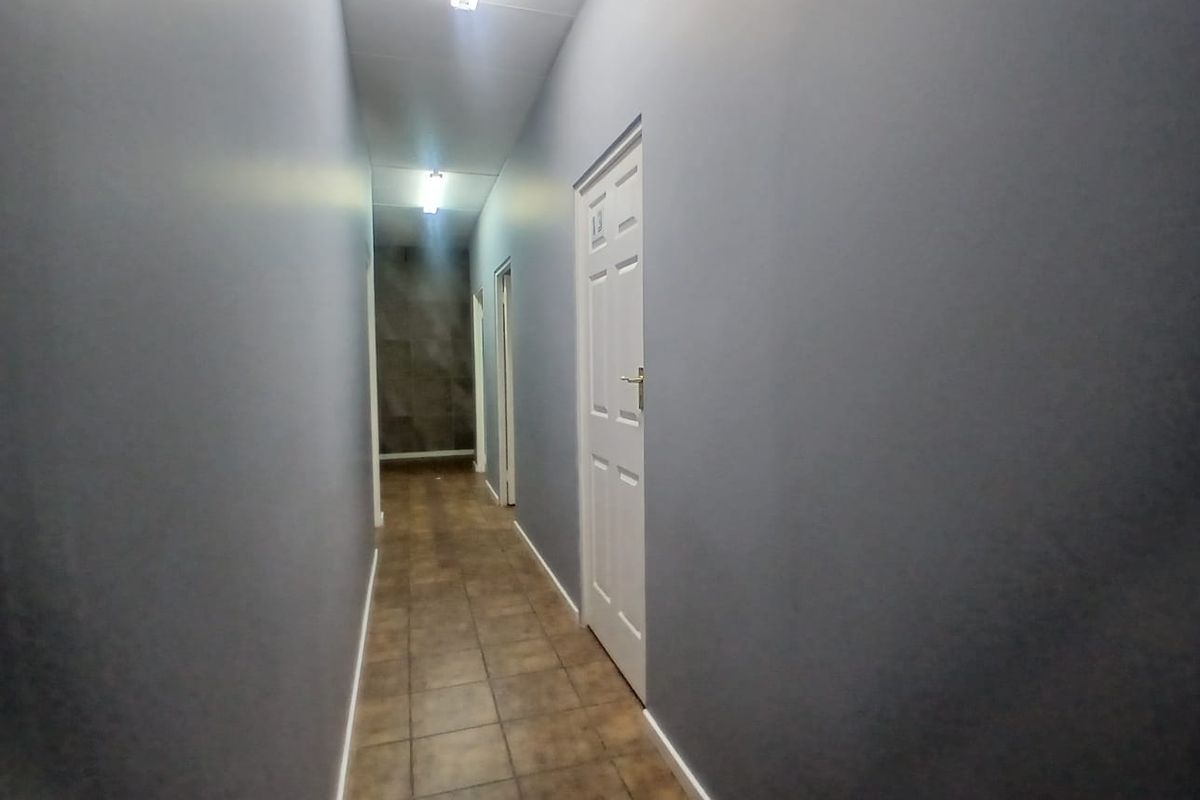A clean, empty office hallway featuring grey painted walls, tiled flooring, and multiple access doors.