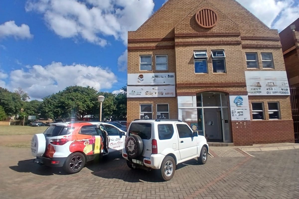 Front exterior view of a two-story face brick office building with a paved parking area and prominent signage.