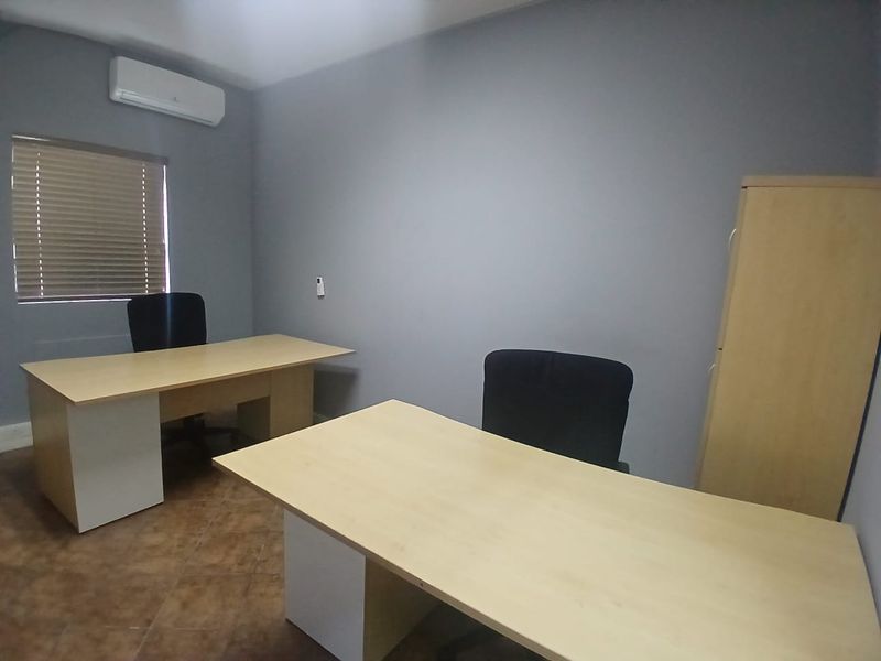 A functional office space featuring tiled flooring, a wall-mounted air conditioning unit, and window blinds, providing a clean and professional work environment.
