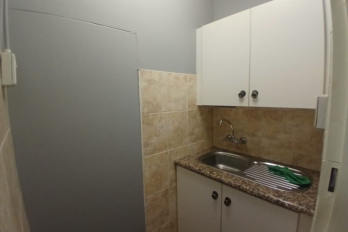 A compact kitchenette area featuring built-in white cabinetry, a stainless steel sink, and a tiled backsplash.