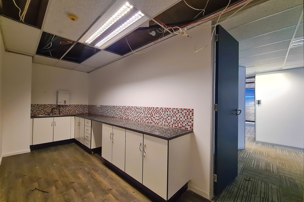 Office kitchenette featuring built-in cabinetry, mosaic tile backsplash, and sink, currently requiring ceiling repairs and general maintenance.