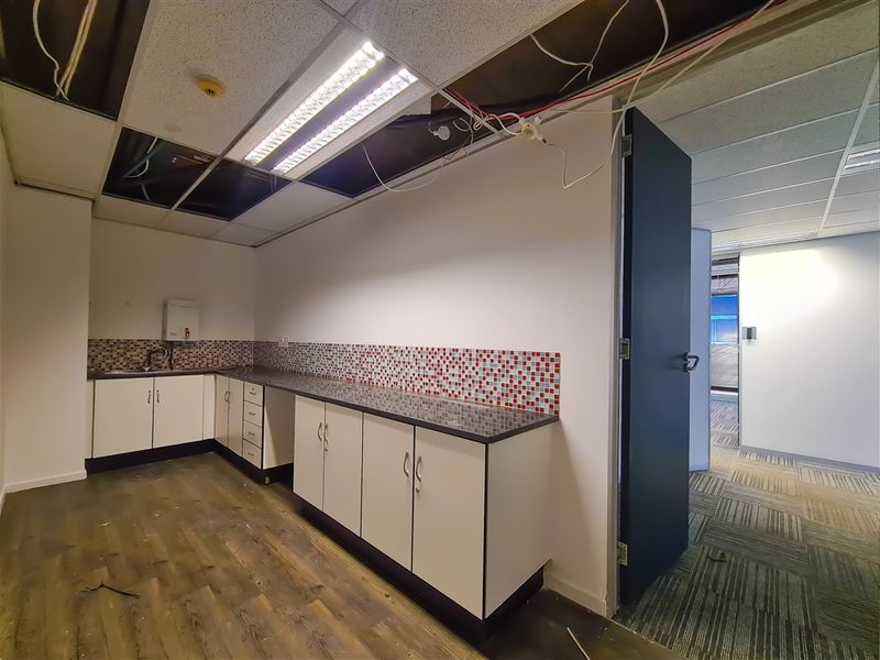 Office kitchenette featuring built-in cabinetry, mosaic tile backsplash, and sink, currently requiring ceiling repairs and general maintenance.