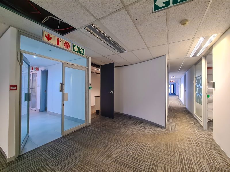 A commercial office hallway featuring carpet tiles, suspended ceilings with integrated lighting, and glass partition doors leading to individual office spaces.