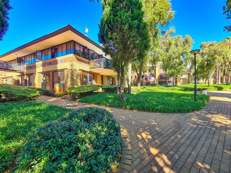 A well-maintained office complex exterior featuring brick architecture, private balconies, and landscaped garden areas with paved walkways.