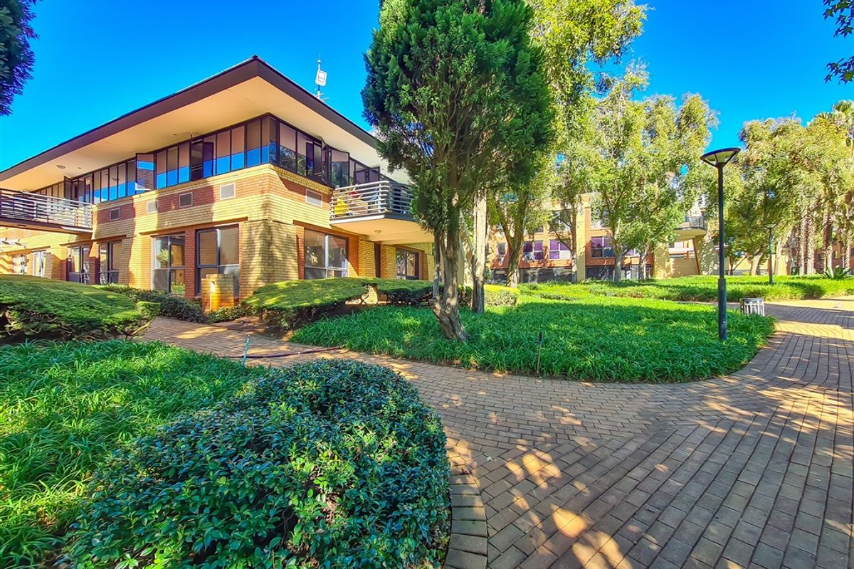 A well-maintained office complex exterior featuring brick architecture, private balconies, and landscaped garden areas with paved walkways.