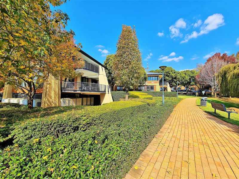 A well-maintained office park exterior featuring a paved walkway, manicured hedges, and multi-story buildings with balconies.