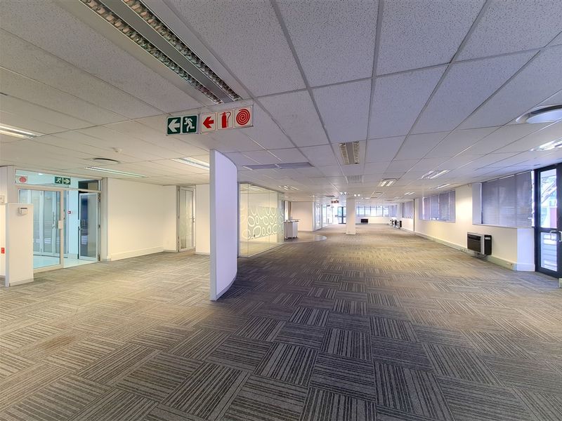 Spacious open-plan office area featuring suspended ceilings, recessed lighting, durable carpet tiles, and glass partitioning, offering a versatile and well-lit professional workspace.