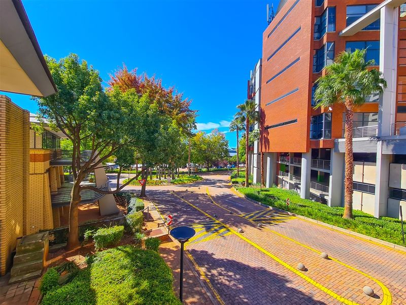 An elevated view of a well-maintained office park entrance featuring brick-paved driveways, landscaped greenery, and modern multi-story brick office buildings.