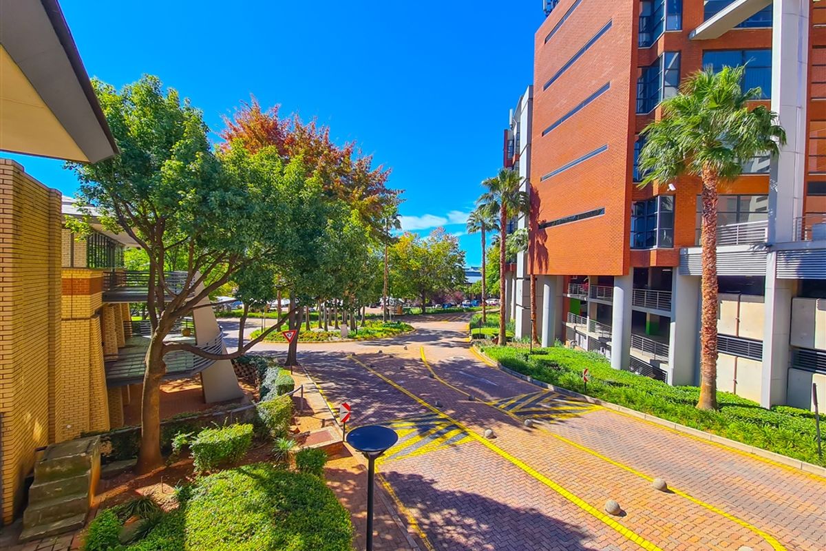 An elevated view of a well-maintained office park entrance featuring brick-paved driveways, landscaped greenery, and modern multi-story brick office buildings.