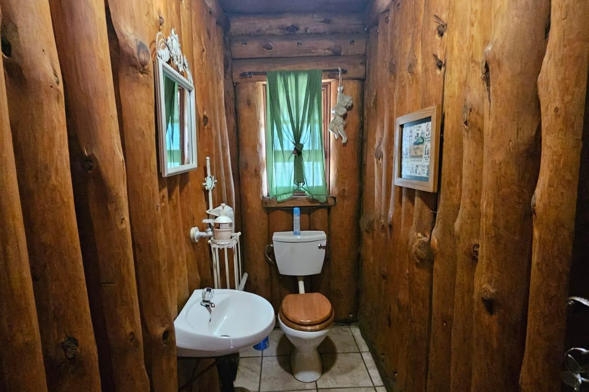A rustic bathroom featuring unique vertical log wall paneling, a standard ceramic toilet, and a wall-mounted basin with tiled flooring.