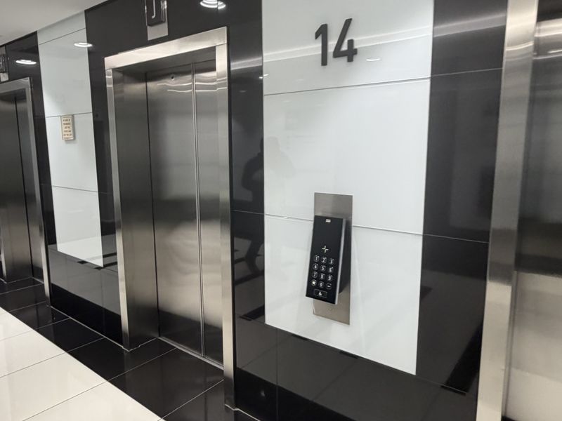 Modern office building elevator lobby featuring high-gloss black and white wall paneling, stainless steel elevator doors, and integrated digital access controls.