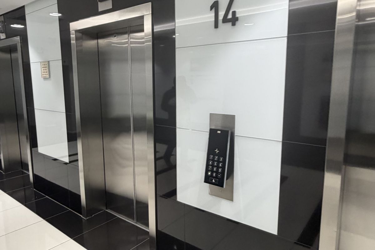 Modern office building elevator lobby featuring high-gloss black and white wall paneling, stainless steel elevator doors, and integrated digital access controls.