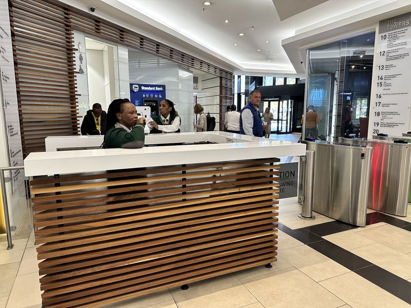 Modern office building lobby featuring a timber-slatted reception desk, secure turnstile access, and a professional directory board for building tenants.