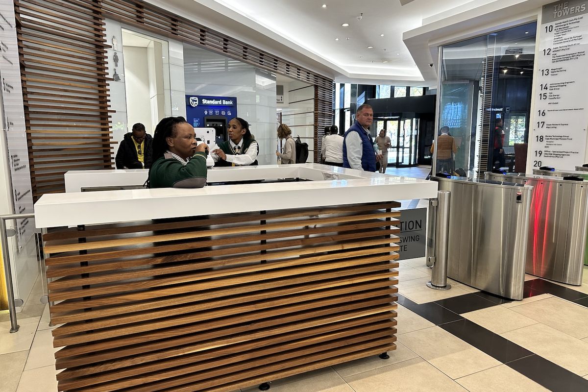 Modern office building lobby featuring a timber-slatted reception desk, secure turnstile access, and a professional directory board for building tenants.