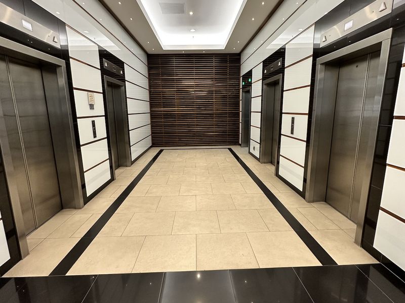 Modern office building elevator lobby featuring high-end finishes, stainless steel elevator doors, decorative slatted wood wall, and sophisticated recessed lighting.