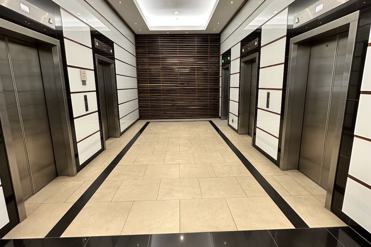 Modern office building elevator lobby featuring high-end finishes, stainless steel elevator doors, decorative slatted wood wall, and sophisticated recessed lighting.