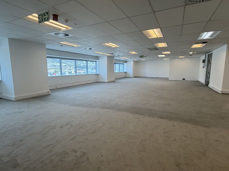 A spacious, open-plan office area featuring a suspended ceiling, recessed lighting, and large windows with city views, currently awaiting floor finishes.