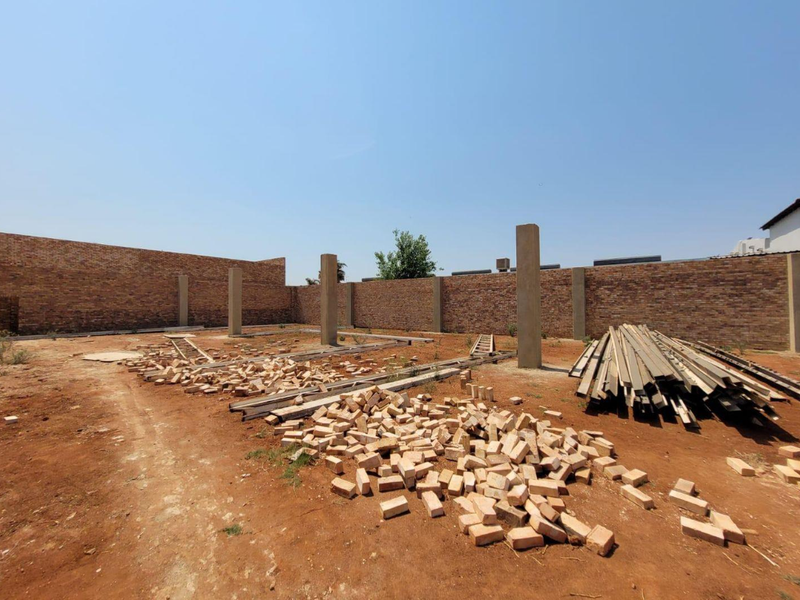 An undeveloped retail property site featuring perimeter brick boundary walls and concrete structural columns on an unpaved ground surface.