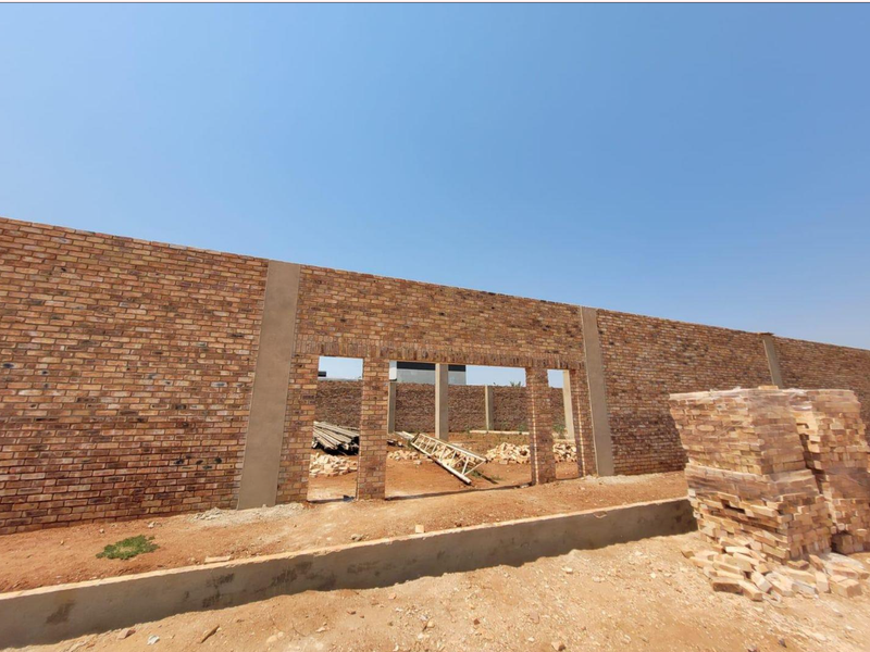 A view of a property under construction featuring a long face brick wall and concrete foundation elements.