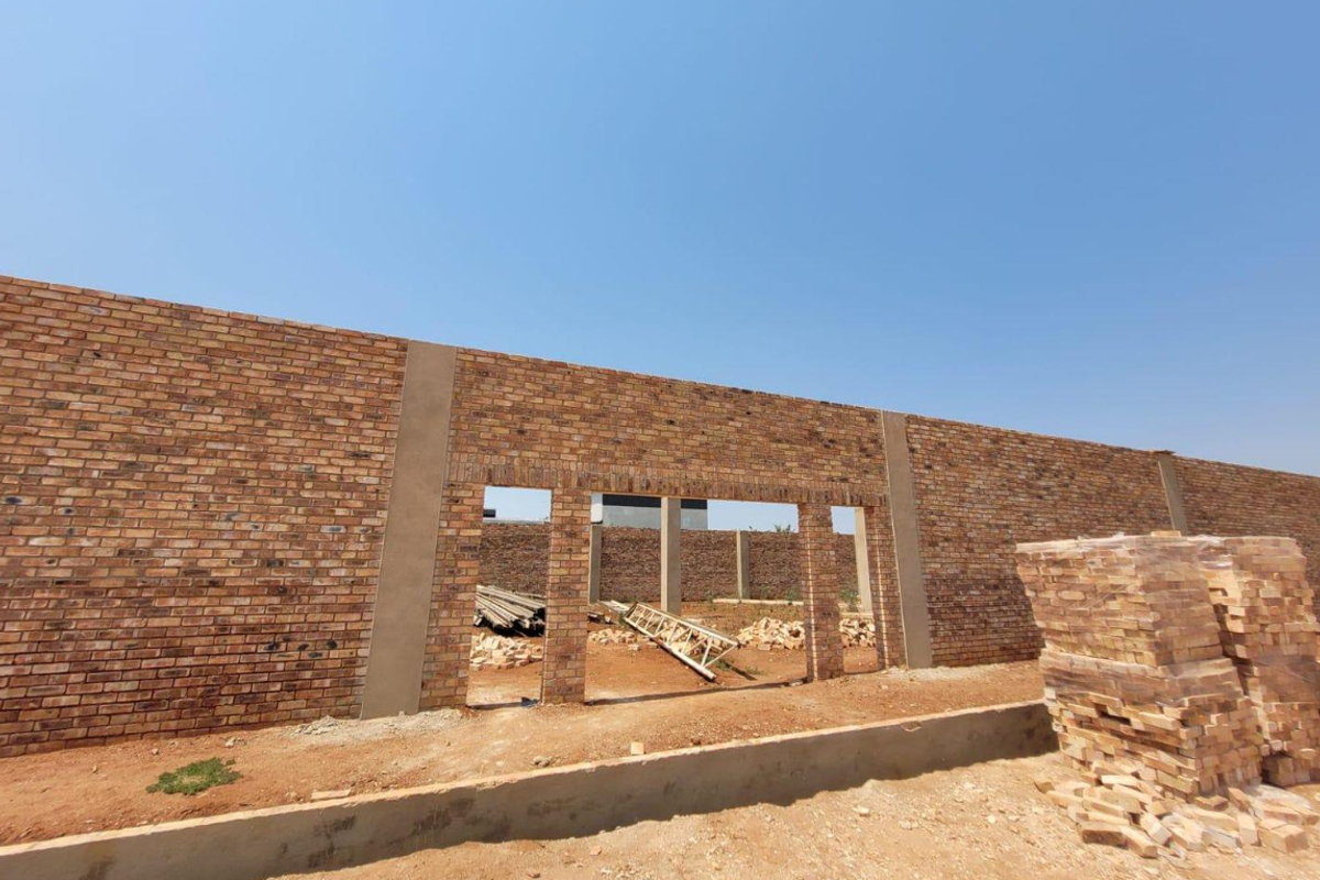 A view of a property under construction featuring a long face brick wall and concrete foundation elements.