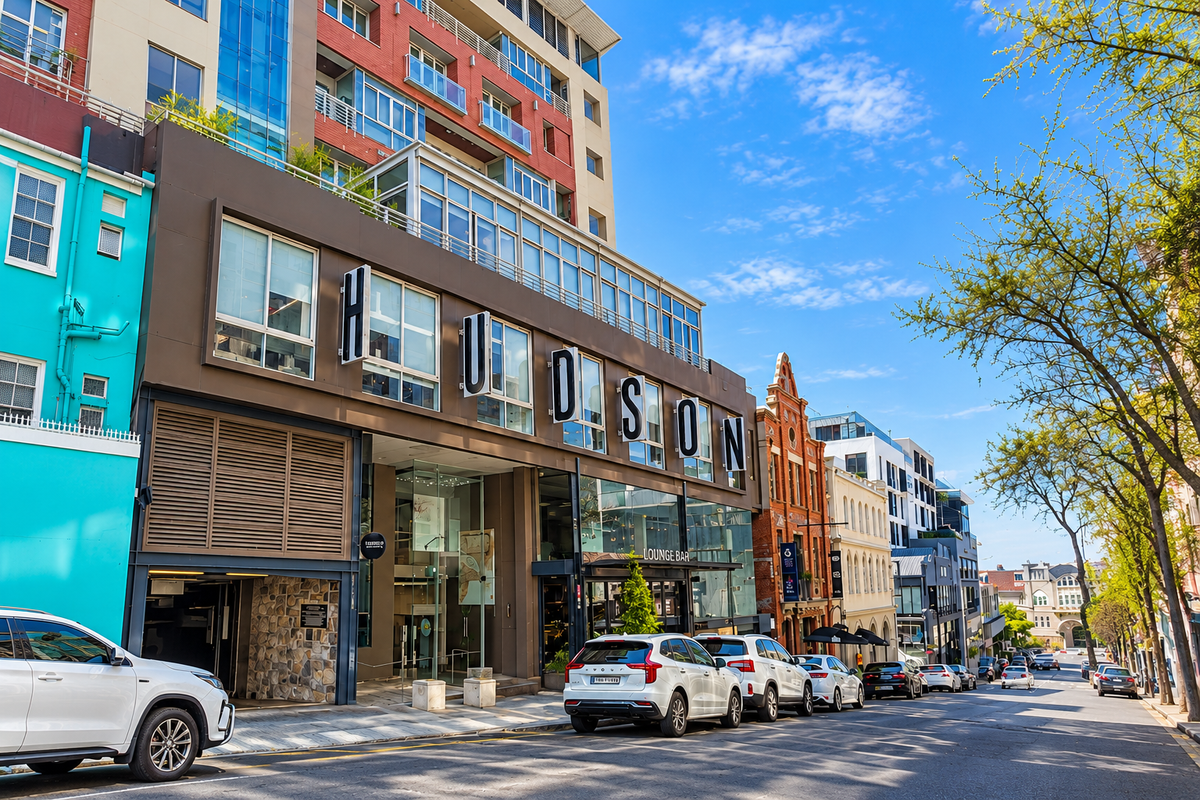 Street-level view of The Hudson building, featuring a modern multi-story facade with large windows, stone detailing, and an integrated parking entrance.
