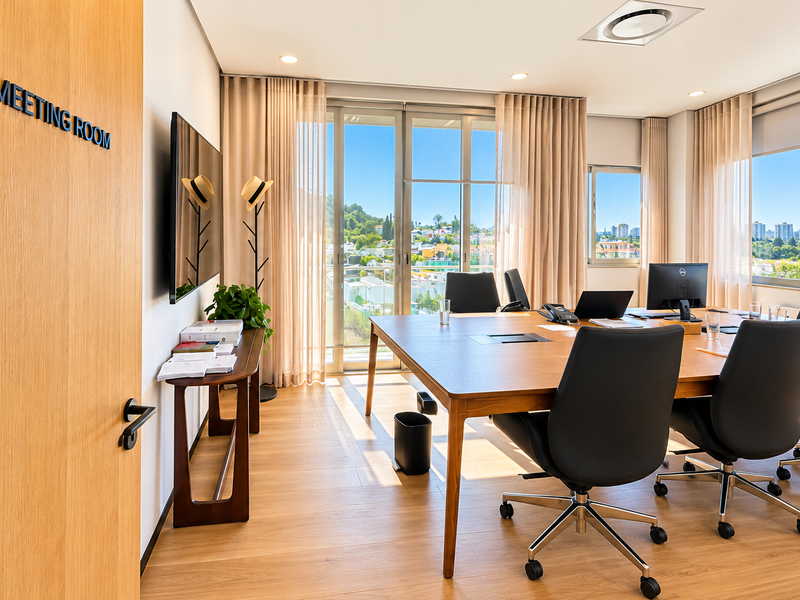 A modern, well-lit office meeting room featuring wood flooring, large glass doors with natural light, and integrated ceiling lighting.