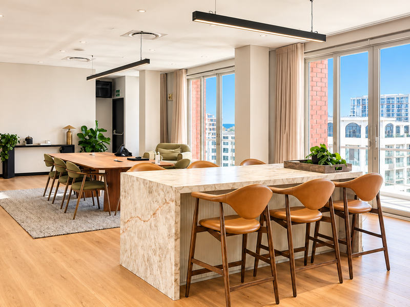 Modern, high-end office space featuring a marble-topped island, hardwood flooring, and expansive floor-to-ceiling windows with natural light and city views.